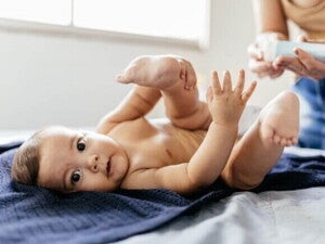 Um bebê deitado de costas em uma toalha azul escura, olhando para a câmera com as pernas levantadas e as mãos abertas, em um momento de troca de fraldas.