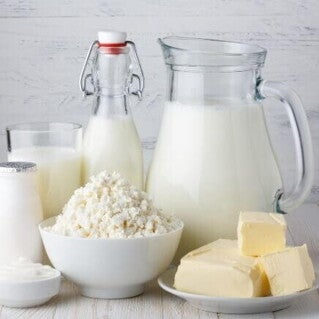 Imagem com leite, queijo, manteiga e outros derivados do leite dispostos sobre uma mesa clara, representando alimentos associados à proteína do leite.