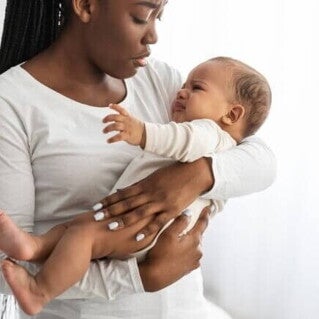 Mãe segura seu bebê que está chorando e visivelmente desconfortável, o que pode ser um sinal de desconforto gastrointestinal ou outros sintomas de APLV.