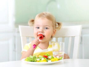 Pequeña comiendo verduras durante la comida.