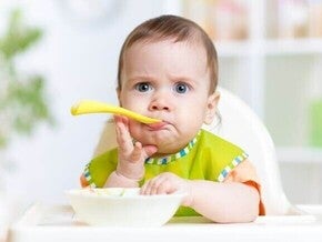 criança sentada em uma cadeira de alimentação com expressão curiosa enquanto come.