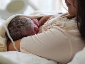Uma mãe recém-parturiente, usando um roupão hospitalar, amamentando seu bebê recém-nascido. Uma mãe recém-parturiente, usando um roupão hospitalar, amamentando seu bebê recém-nascido.