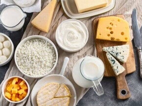 Visão aérea de uma mesa repleta de produtos lácteos variados. Os alimentos estão dispostos sobre um pano bege.