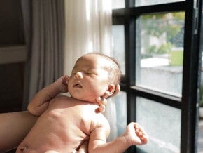 Bebê tomando banho de sol através da luz de uma janela