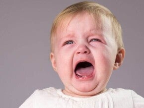 bebê loiro de olhos claros chorando com a boca aberta e expressão de desconforto.