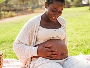 Mulher grávida sorrindo sentada na grama e acariciando a barriga