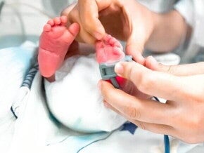 Pés de um bebê recém-nascido passando por uma avaliação pelas mão de um profissional da saúde.