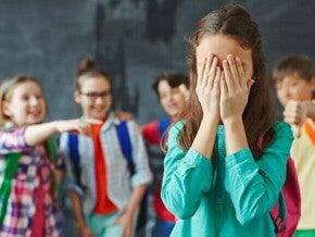 Grupo de crianças apontando e rindo de uma menina que está cobrindo o rosto com as mãos