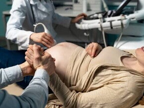 Uma gestante deitada em um consultório médico, segurando a mão de um homem, durante um exame de ultrassom