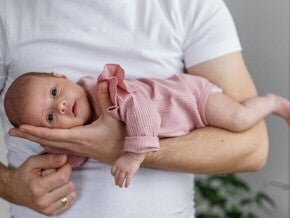 Como aliviar gases em recém nascido Close-up de um pai segurando um recém-nascido com a barriga para baixo em seu antebraço, em uma posição de "avião".