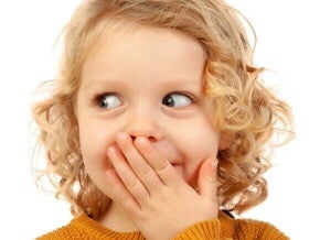 Criança pequena com expressão de vergonha ou timidez, cobrindo a boca.