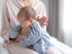 Posição clássica de como fazer para bebe arrotar: a mãe segura o bebê confortavelmente contra o ombro com um pano de boca para protegê-la contra golfadas de leite ou saliva.