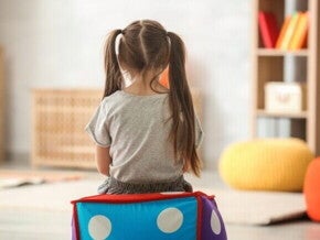 Criança sentada em cubo colorido em sala de terapia infantil, vista de costas.