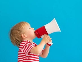 Um menino loiro usando camiseta listrada segura um megafone vermelho e branco contra um fundo azul sólido.