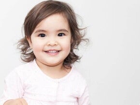 Bebê sorrindo, vestindo uma roupa rosa em um fundo branco.