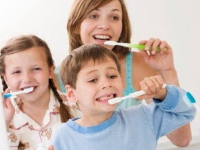 Uma foto de uma mãe e seus filhos, sorrindo e escovando os dentes juntos no banheiro. A imagem sugere uma maneira divertida de como ensinar crianças a escovar os dentes.