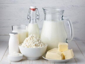 Imagem com leite, queijo, manteiga e outros derivados do leite dispostos sobre uma mesa clara, representando alimentos associados à proteína do leite.