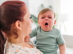 Mãe segurando um bebê que chora, com a boca aberta, indicando dor ou desconforto, possivelmente devido à faringite em bebês ou outra inflamação na garganta.