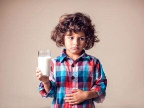 Intolerância à lactose em crianças: como identificar? Imagem de uma criança desconfortável, com um copo de leite em uma mão e outra sobre a barriga em uma postura que remete aos efeitos da intolerância à lactose.