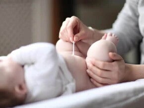 Mamãe limpando o cordão umbilical do bebê com um cotonete.