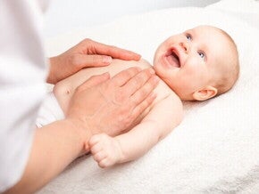 massagem shantala para bebê, com o bebê sorrindo e o adulto aplicando a massagem no peito.