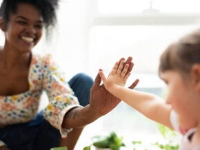 mulher negra com um largo sorriso e uma blusa floral dá um "toca aqui" a uma criança pequena, que estende a mão em resposta