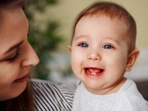 Bebê sorrindo no colo da mãe, com os primeiros dentinhos visíveis, ilustrando o processo do nascimento dos dentes do bebê.