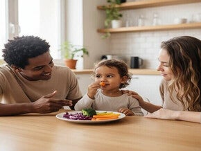 Criança brasileira de 4 anos experimentando novos legumes com os pais na cozinha.