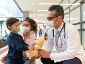 Neuropediatra Neuropediatra e enfermeira se aproximam de uma criança, que segura um urso de pelúcia.