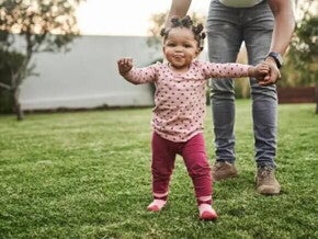 O que é coordenação motora e quais suas fases nas crianças Menina aprendendo a andar e ganhando coordenação motora. Ela caminha no quintal orientada pela mãe, que segura a sua mão esquerda.