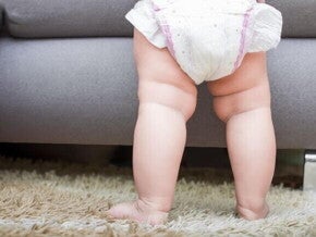 Imagem das pernas de um bebê em pé, em cima de um tapete