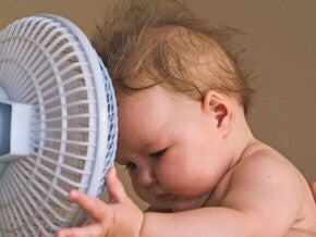 Um bebê com a cabeça próxima a um pequeno ventilador Um bebê com a cabeça próxima a um pequeno ventilador