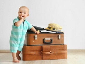 Bebê sorrindo, com a mão na boca, apoiado em malas de viagem. Bebê sorrindo, com a mão na boca, apoiado em malas de viagem.