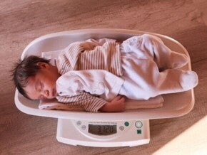 Um bebê recém-nascido dormindo sobre uma balança digital que mostra o peso. A imagem ilustra o monitoramento do peso do bebê, um tema central para a perda de peso neonatal. Um bebê recém-nascido dormindo sobre uma balança digital que mostra o peso. A imagem ilustra o monitoramento do peso do bebê, um tema central para a perda de peso neonatal.