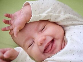 Close de um bebê recém-nascido deitado, com os olhos fechados e uma expressão de felicidade. Ele usa um macacão branco com bolinhas pretas e está com a mãozinha sobre a testa.