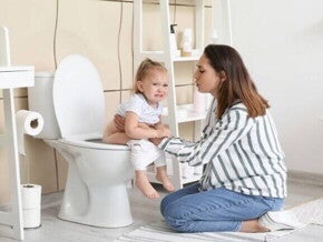 Mãe consolando uma criança pequena que chora e está sentada no vaso sanitário, ilustrando o desconforto e preocupação associados a problemas intestinais ou a presença de sangue nas fezes de criança.