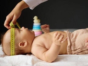 Um bebê deitado, com a cabeça sendo medida por outra pessoa com uma fita métrica.