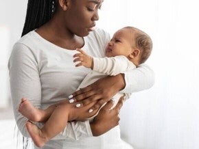 Mãe segura seu bebê que está chorando e visivelmente desconfortável, o que pode ser um sinal de desconforto gastrointestinal ou outros sintomas de APLV.