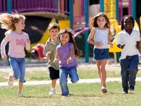 Cinco crianças correndo juntas e sorrindo em um parque gramado. A imagem transmite alegria, vitalidade e saúde, associadas ao tema do suplemento alimentar infantil.