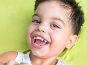 Menino em cima da cama com roupa branca sorrindo
