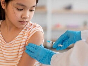 Uma criança recebendo uma injeção no braço de um profissional de saúde usando luvas azuis, simbolizando a aplicação da vacina HPV.