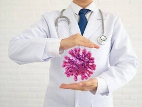 Um profissional da saúde em pé, com uma ilustração de um vírus colocada entre as suas mãos.