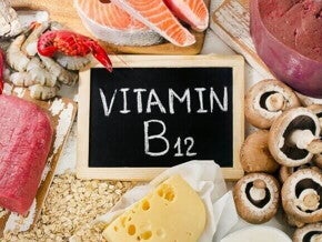 Uma composição de alimentos ricos em vitamina B12, com um pequeno quadro negro no centro com a inscrição "Vitamina B12" em giz. 