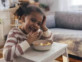 Foto de uma criança fazendo um lanche e comendo com as mãos uma vasilha de salada de frutas, um exemplo de alimento rico em vitamina C Foto de uma criança fazendo um lanche e comendo com as mãos uma vasilha de salada de frutas, um exemplo de alimento rico em vitamina C