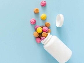 Vitaminas para criança Visão de cima de gomas de vitaminas coloridas, em formato de espiral ou flor, que caíram de um pote branco sem rótulo, sobre uma superfície azul clara.