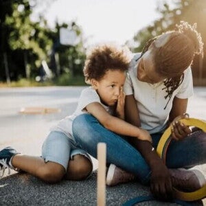 Mãe e filho, uma criança de 6 anos, estão sentados no chão de um espaço ao ar livre. A mãe olha para o filho, que o abraça. Mãe e filho, uma criança de 6 anos, estão sentados no chão de um espaço ao ar livre. A mãe olha para o filho, que o abraça.