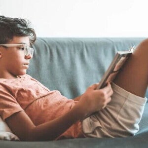 Criança de 7 anos lendo um livro deitada em um sofá, apoiada em uma almofada. Criança de 7 anos lendo um livro deitada em um sofá, apoiada em uma almofada.