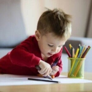 Criança pequena colorindo uma folha branca, aprendendo cores.