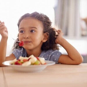 Menina vegetariana comendo um prato de frutas