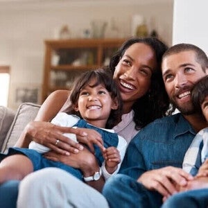 Família com dois filhos em idade escolar assistindo TV juntos em casa.